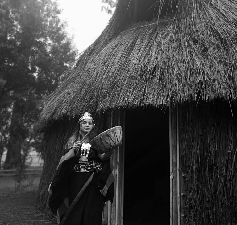 FOTO GANADORA EN CATEGORÍA COSTUMBRES - Fotografía en blanco y negrode Mapuche mujer tocando instrumento musical